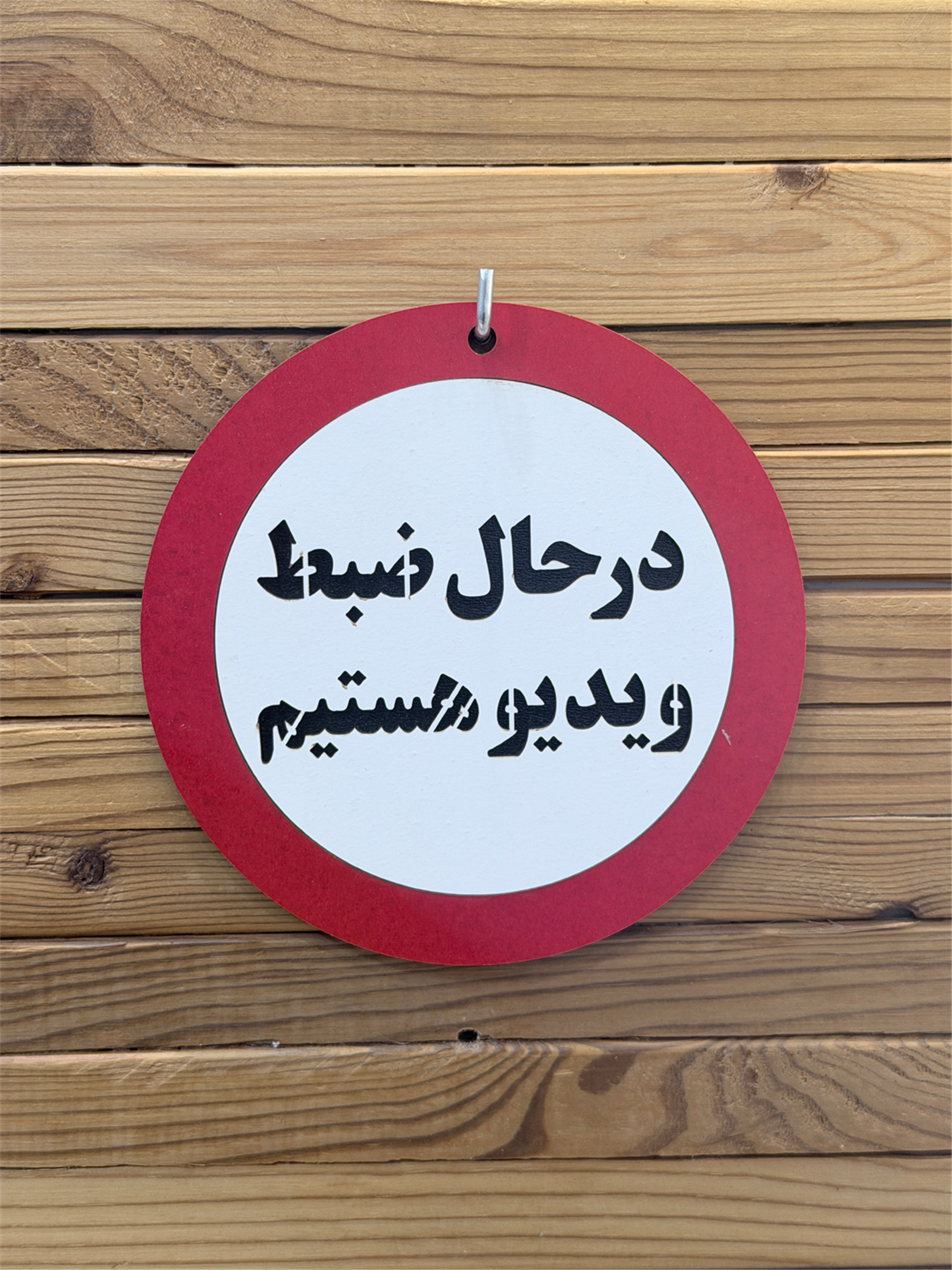 نمای روبرو تابلو چوبی "در حال ضبط ویدیو هستیم" با حاشیه قرمز